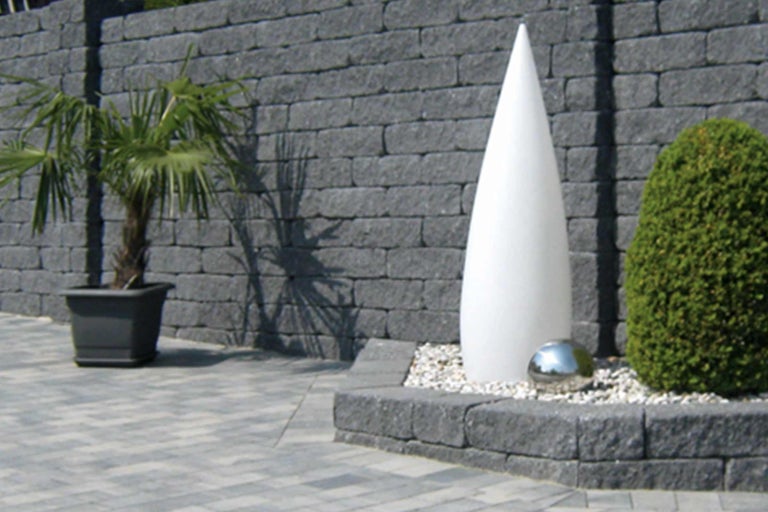 Garten mit Mauer aus Mauersteinen, Pflanze im Topf, Dekoelementen und Pflastersteinen.