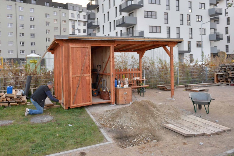 Mann streicht Holzgartenhaus im Gartenbereich vor Wohngebäuden