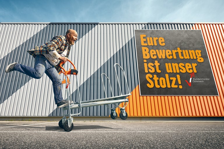 Ein Mann fährt mit einem Transportwagen vor einer Wand, auf der der Spruch Ihre Bewertung ist unser Stolz steht.