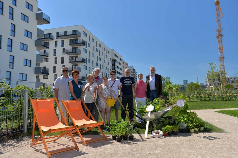 Gruppe von Personen mit Gartenwerkzeugen und Pflanzen vor einem Wohngebäude