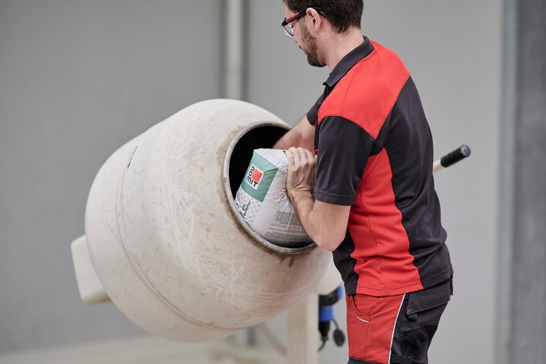 Ein Mann schüttet einen Sack Beton in einen Betonmischer.