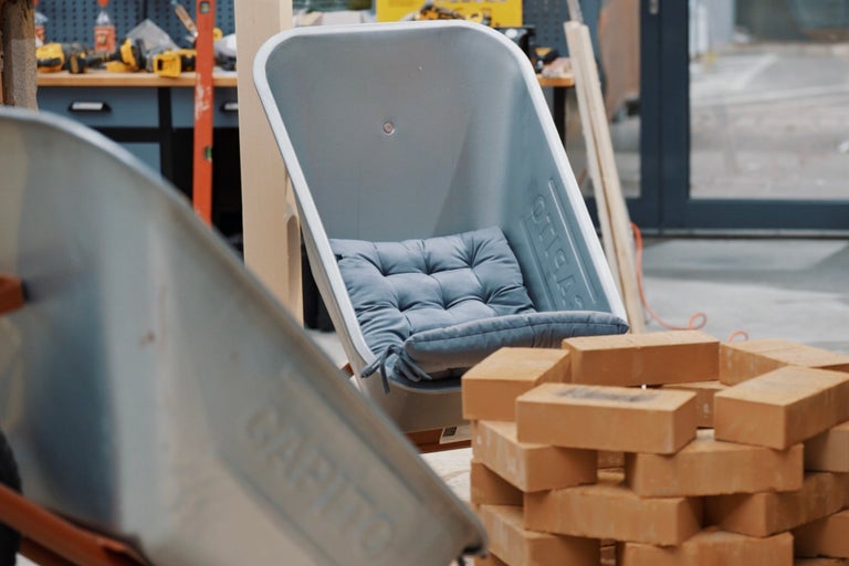 Szene mit einer Schubkarre, umgewandelt in einen Stuhl mit Kissen, und einem Stapel Ziegelsteine.