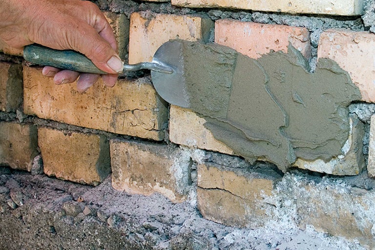 Maurerhandwerker trägt Mörtel mit einer Maurerkelle auf eine Ziegelwand auf.