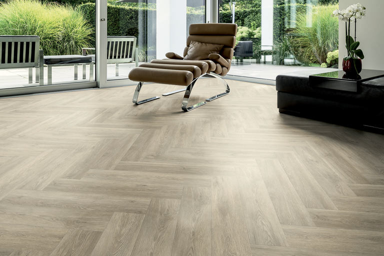 Heller Raum mit verlegtem Vinylboden im Fischgrätmuster, Sessel und Terrassentür