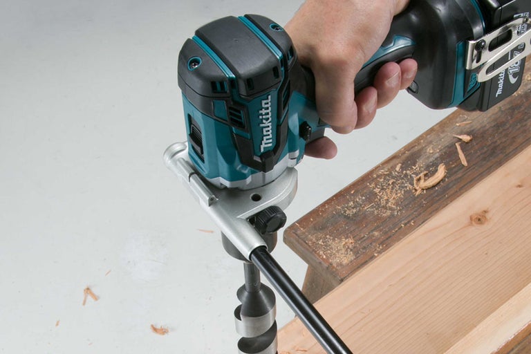 Makita Logo. Akku-Bohrmaschine im Einsatz beim Bohren eines Lochs in ein Holzbrett.