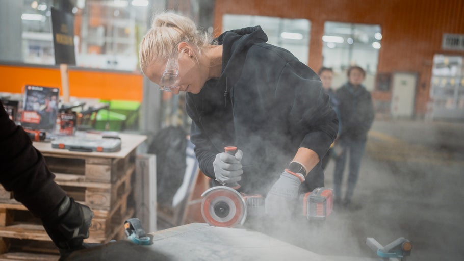Frau schneidet Material mit einem Winkelschleifer, Schutzbrille und Handschuhe werden getragen
