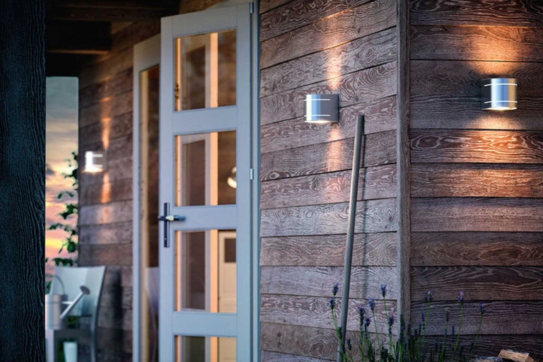 Holzhausfassade mit Außenleuchten neben einer Glastür