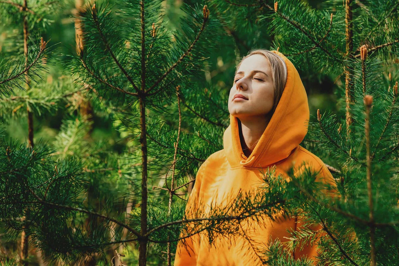 Frau mit geschlossenen Augen in einem Kiefernwald mit Hoodie
