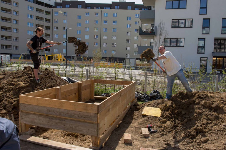 Zwei Personen befüllen ein Hochbeet mit Erde.