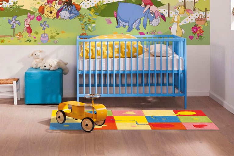 Kinderzimmer mit Kinderbett, Teppich und Spielzeugauto vor einer Winnie Puuh Tapete