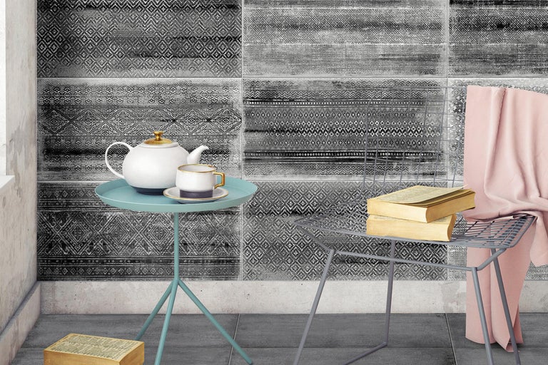 Raumansicht mit gemusterten Fliesen, kleinem Tisch mit Teekanne und Tasse sowie einem Stuhl mit Büchern.