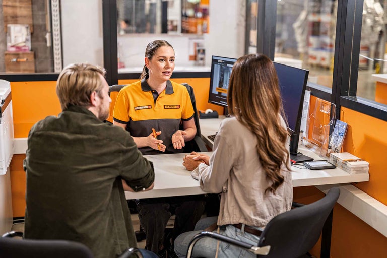 Ein Hornbach Mitarbeiter berät Kunden an einem Schreibtisch.