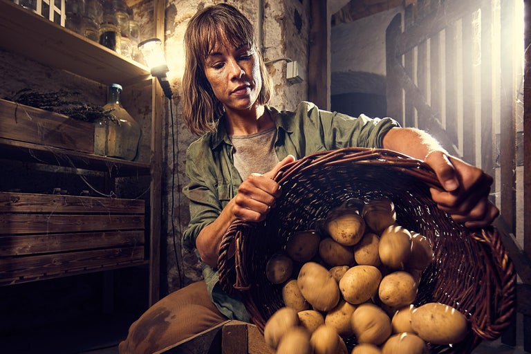 Frau hält Korb mit Kartoffeln im Keller.