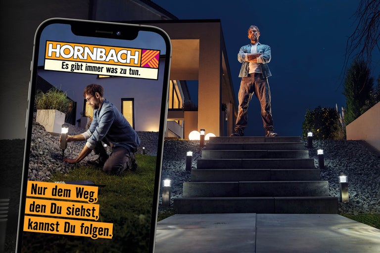 Ein Mann installiert Gartenleuchten entlang einer Steintreppe vor einem Haus bei Nacht, dargestellt auf einem Smartphonebildschirm und in der Szene.