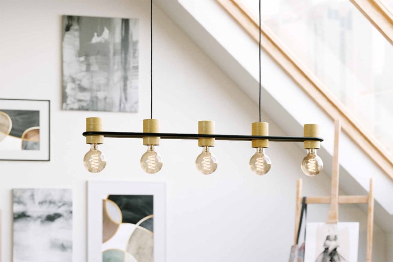 Pendelleuchte mit fünf Lampen und Holzdetails in einem hellen Raum.