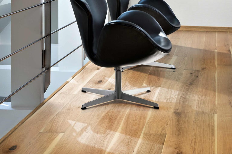 Holzfußboden mit schwarzen Stühlen und Treppengeländer im hellen Raum.