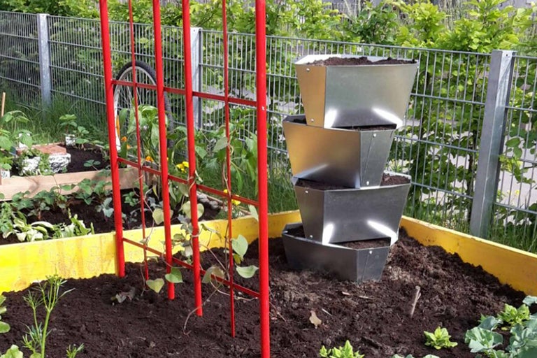 Gestapelte Pflanzgefäße aus Metall und Rankhilfe in einem Gemüsebeet.