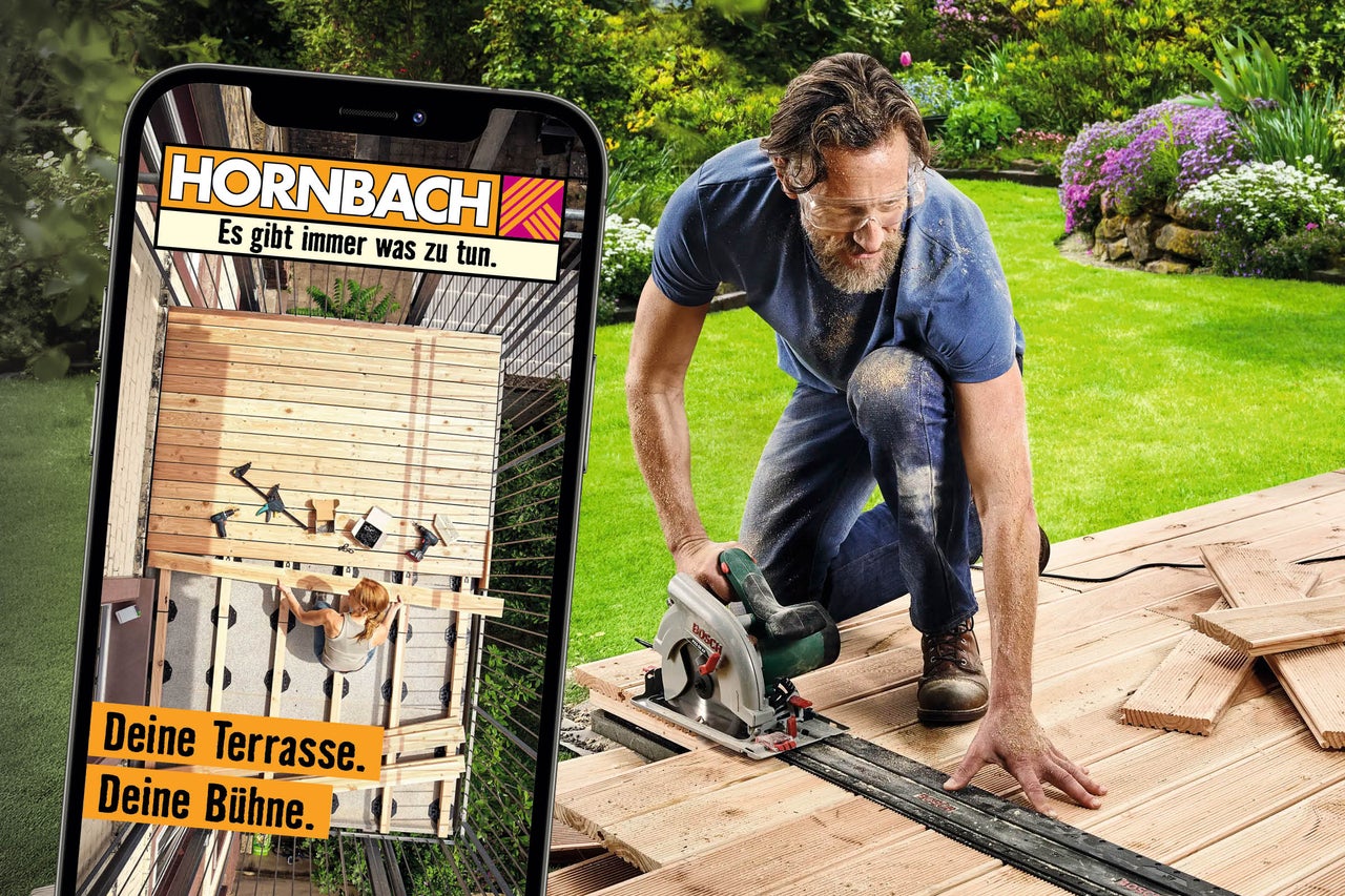 Ein Mann sägt mit einer Handkreissäge Holzdielen auf einer Terrasse, während ein Smartphone das Projekt mit dem Hornbach Logo zeigt.