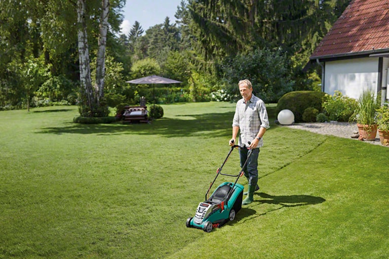 Mann mäht Rasen mit einem Rasenmäher im Garten.