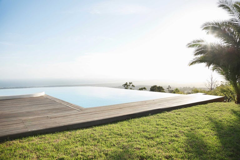 Szene mit einem Pool auf einer Holzterrasse, einem Rasen und Blick auf das Meer