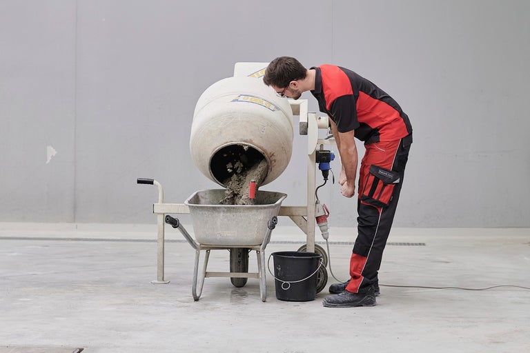 Ein Bauarbeiter befüllt eine Schubkarre mit Beton aus einem Betonmischer.