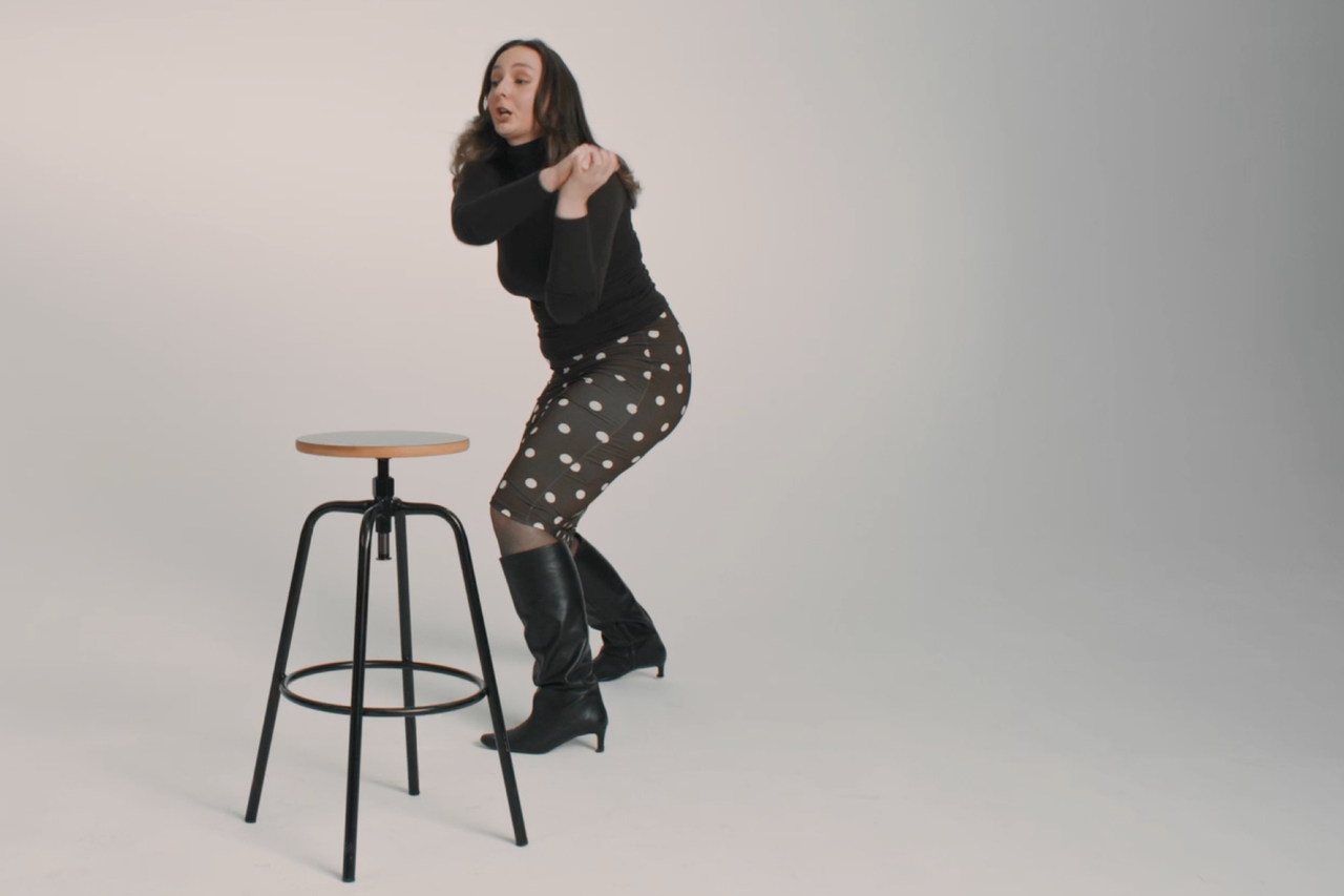 Eine Frau steht neben einem Barhocker mit Holzplatte und Metallgestell.