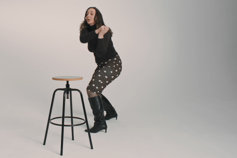 Eine Frau steht neben einem Barhocker mit Holzplatte und Metallgestell.