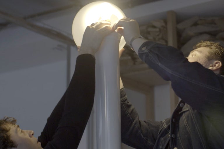 Zwei Personen befestigen eine runde Lampe an einem Lampenfuß