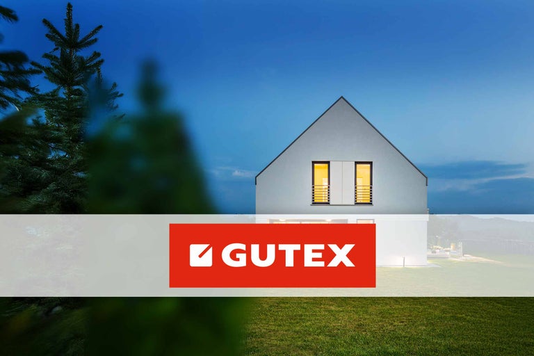 GUTEX Logo vor einem Haus mit beleuchteten Fenstern