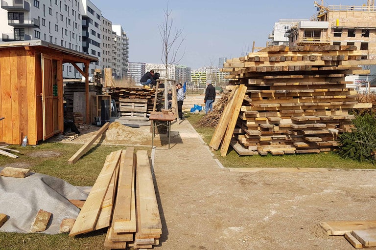 Außenansicht einer Baustelle mit Holzlager und Personen