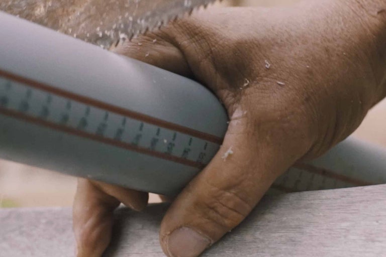 Nahaufnahme eines Mannes, der ein graues Kunststoffrohr mit einer Handsäge schneidet.