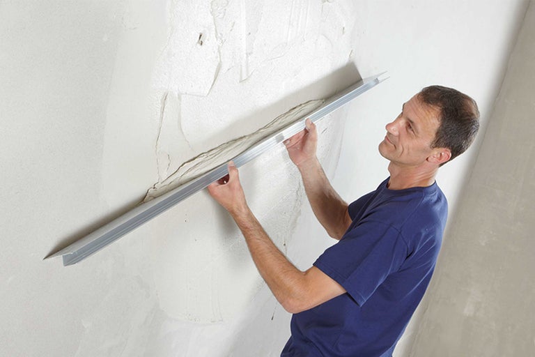 Mann glättet eine Wand mit einer Abziehlehre.