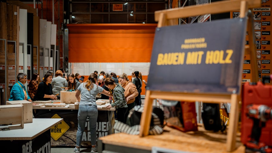 Veranstaltung mit dem Titel Bauen mit Holz in einem Baumarkt, bei der Menschen an Tischen arbeiten