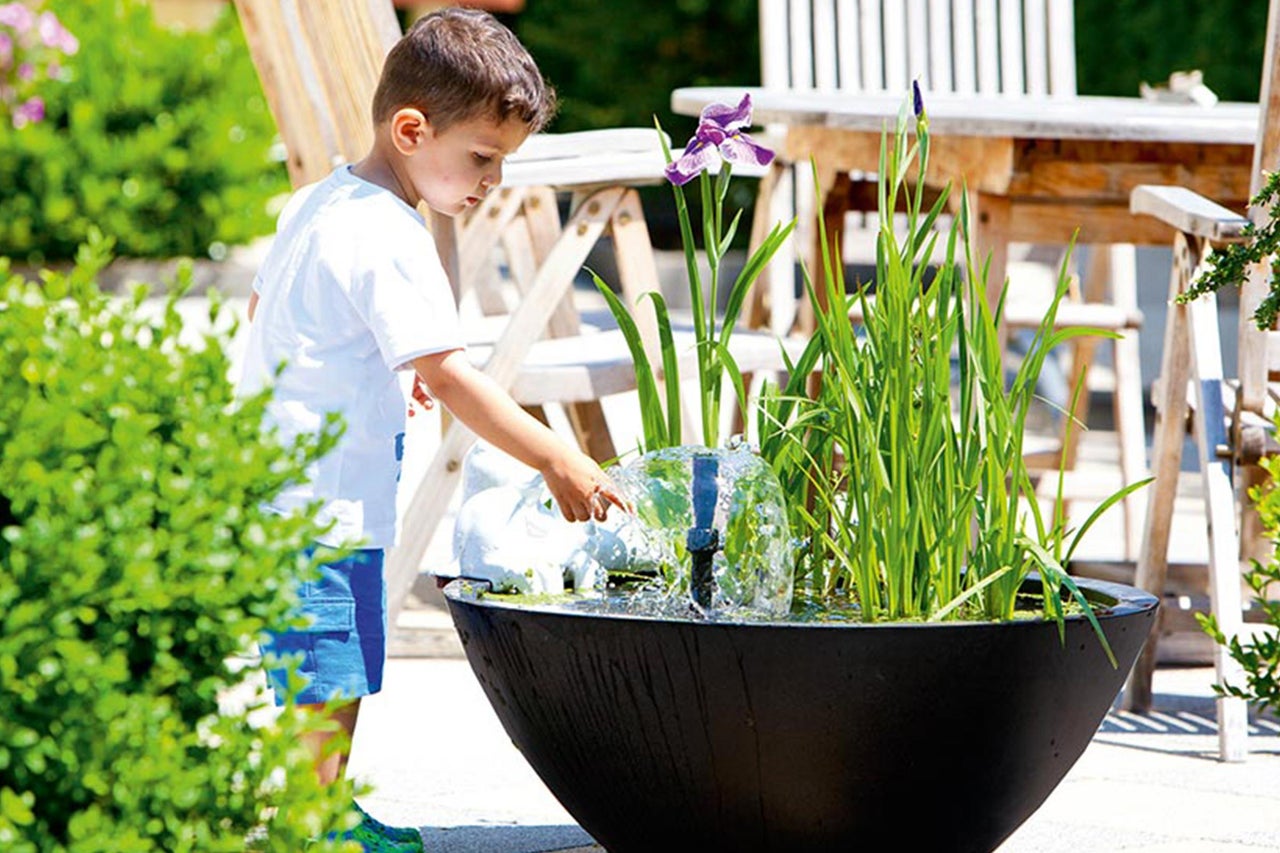 Junge spielt mit einem Springbrunnen im Garten