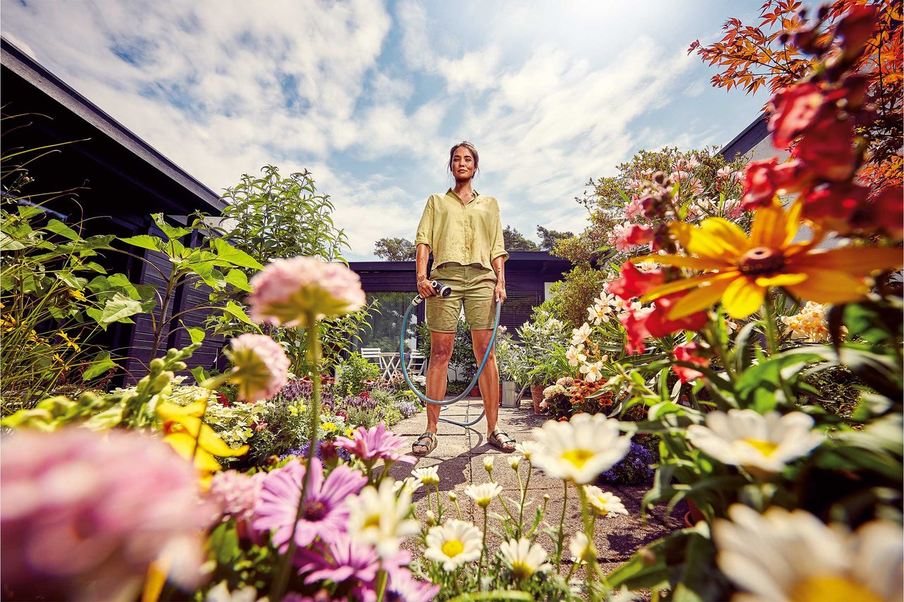 Frau hält Gartenschlauch in blühendem Garten