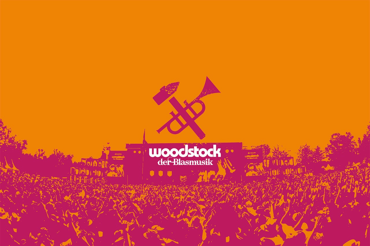 Woodstock der Blasmusik Logo vor einer Festivalbühne und einer großen Menschenmenge.