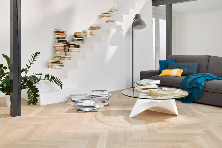 Wohnzimmer mit grauer Couch, Bücherstapeln, runden Glastisch und Treppe