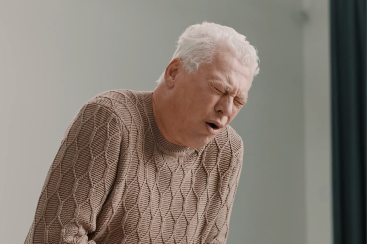 Ein Mann mittleren Alters mit Schmerzen im Gesicht trägt einen braunen Strickpullover.