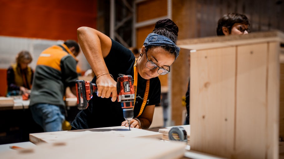 Frau arbeitet mit einem Akku-Bohrschrauber an einem Holzstück.