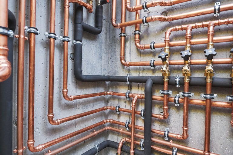 Installation von Heizungsrohren aus Kupfer und isolierten Rohren an einer Wand.