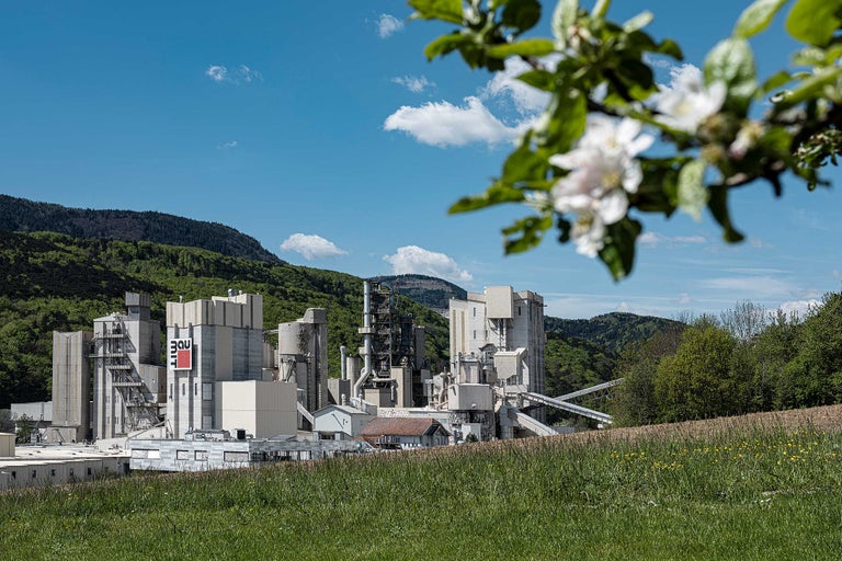 Aussicht auf ein Zementwerk mit einem Logo der Firma Bau-it und einer Berglandschaft im Hintergrund.