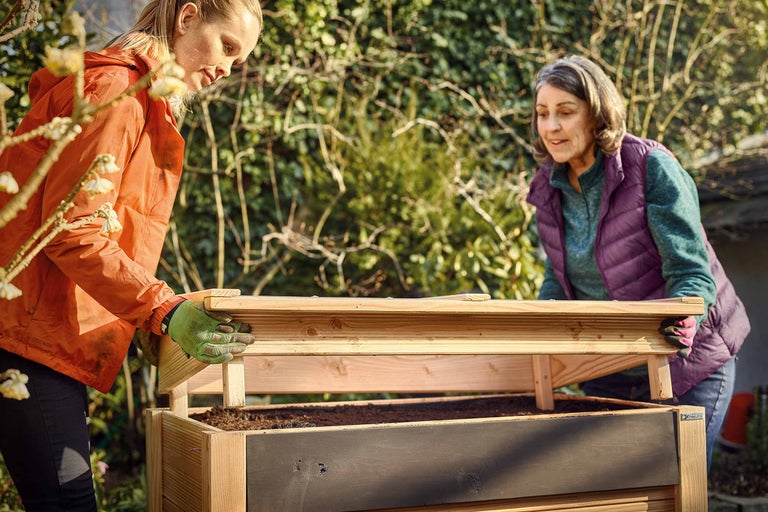 Zwei Frauen öffnen ein Hochbeet im Garten.