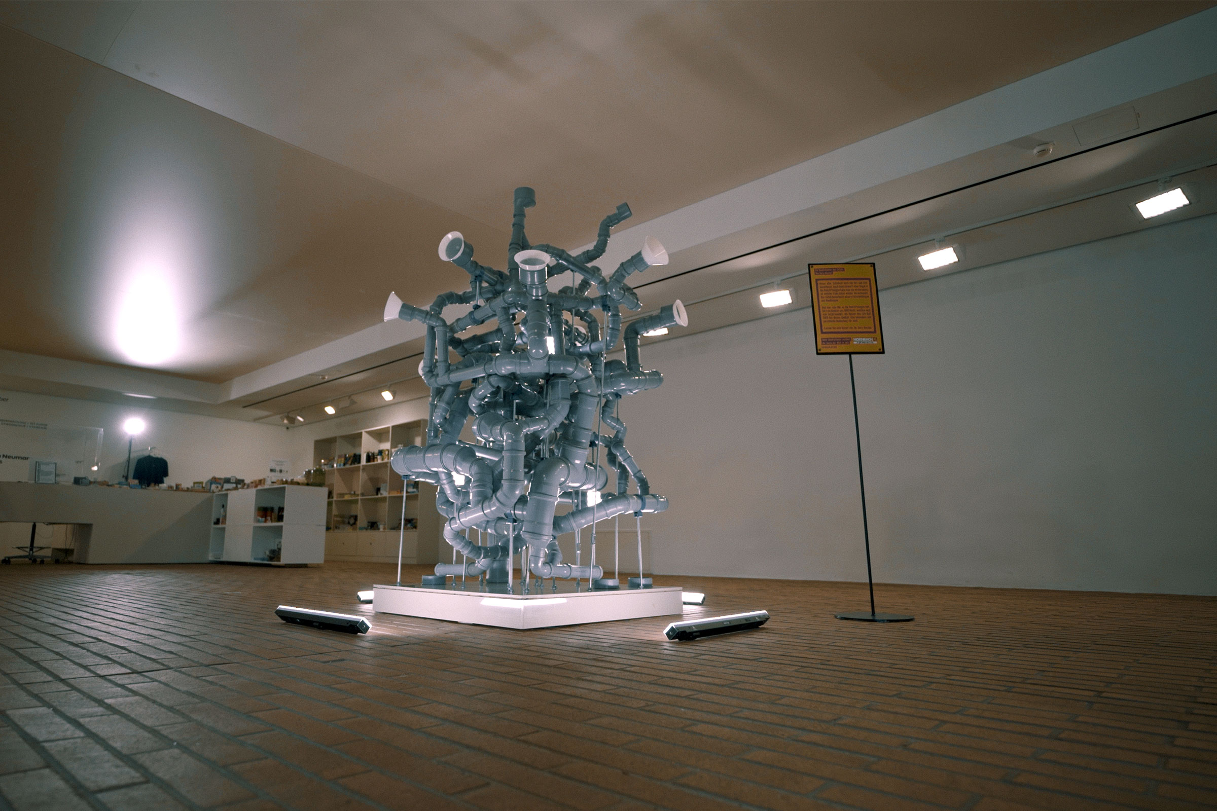 Installation aus grauen Kunststoffrohren und Verbindungsstücken in einem Ausstellungsraum.