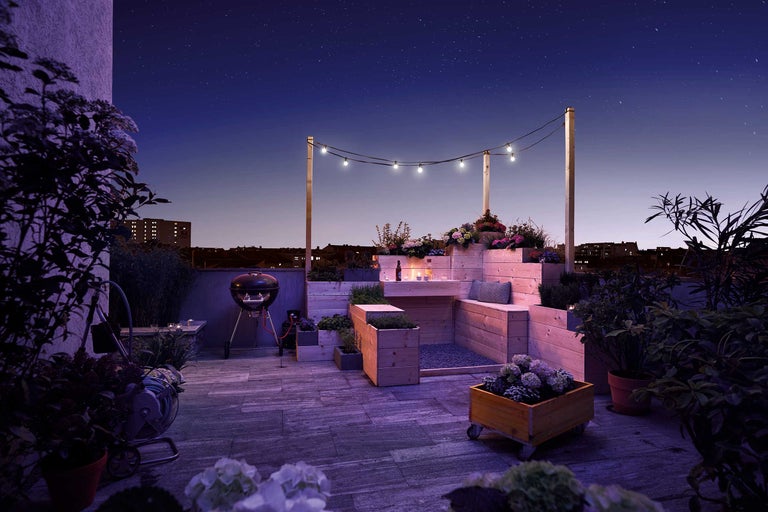 Dekorierter Dachgarten mit Grill, Holzmöbeln und Pflanzen bei Nacht