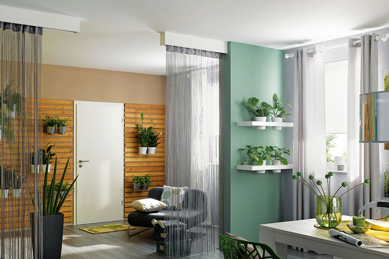 Dekoratives Zimmer mit Pflanzen, Möbeln und Vorhängen für ein gemütliches Ambiente.