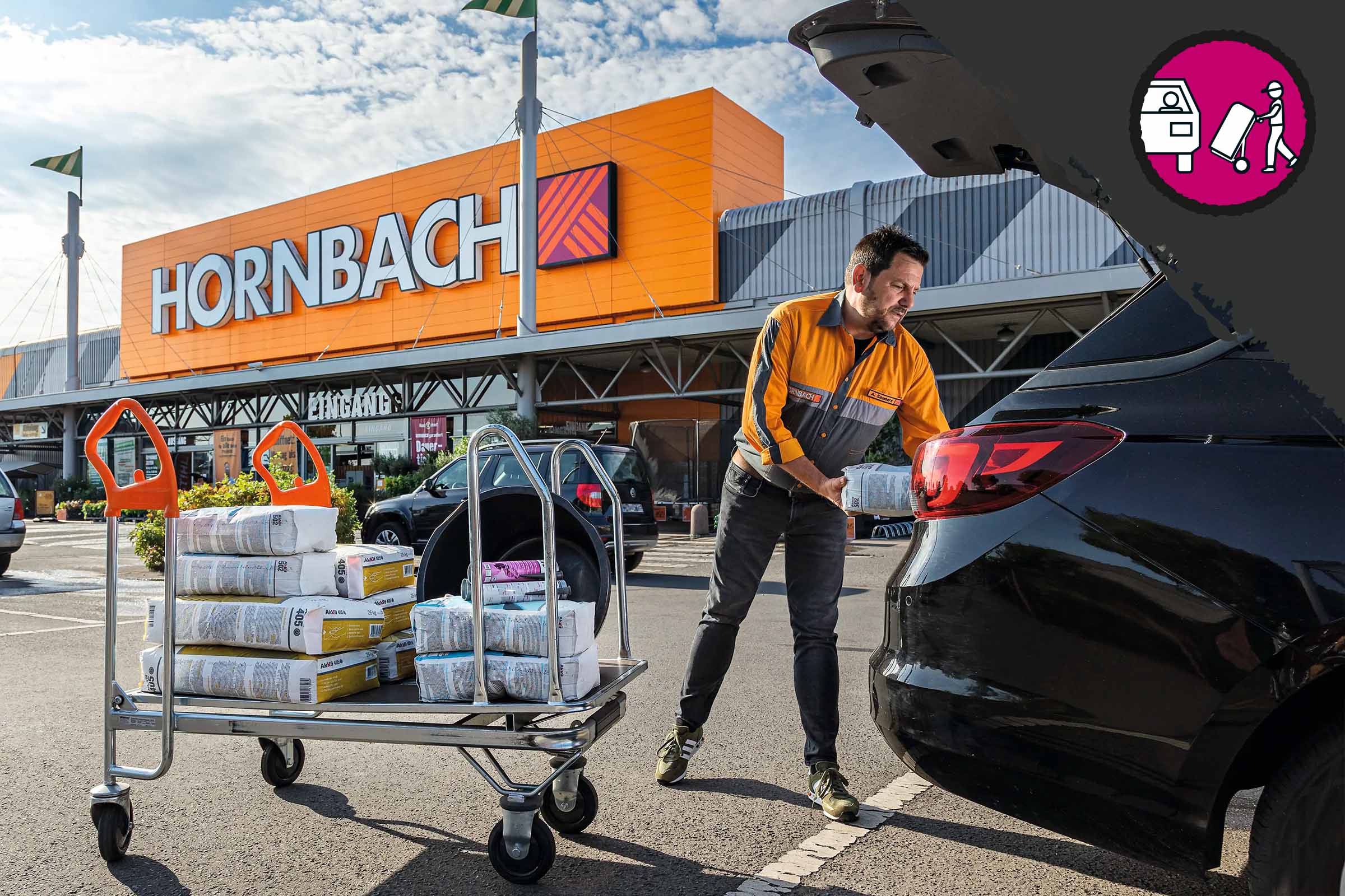 Ein Hornbach Mitarbeiter belädt einen Kofferraum mit Baumaterialien, die auf einem Transportwagen stehen, vor einem Hornbach Baumarkt.