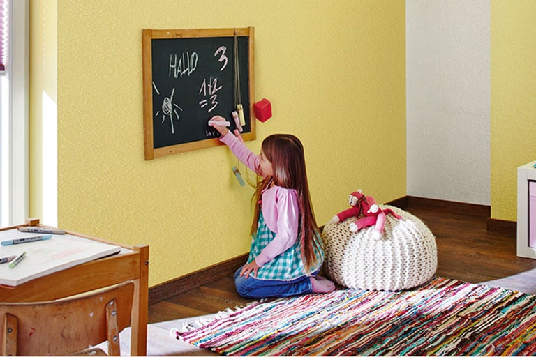 Mädchen schreibt mit Kreide auf eine Tafel im Kinderzimmer
