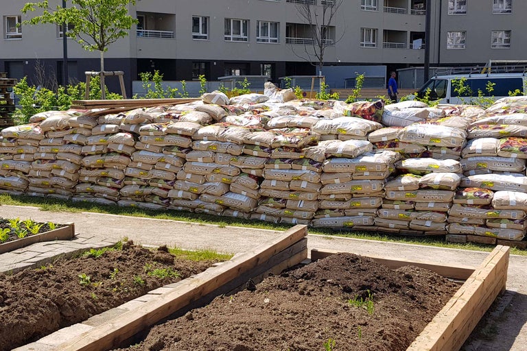 Gestapelte Säcke Pflanzerde neben bepflanzten Hochbeeten im Freien