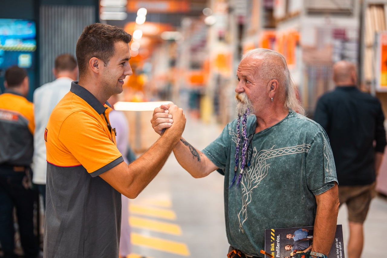 Ein Hornbach Mitarbeiter und ein Kunde begrüßen sich per Händedruck im Baumarkt.