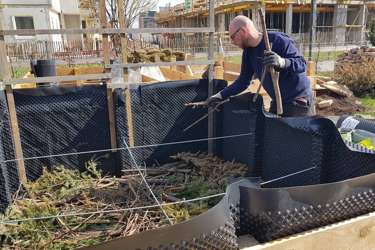 Mann befüllt Hochbeet mit Ästen und Zweigen, ausgekleidet mit Noppenfolie.